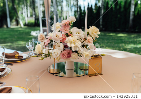 Elegant wedding table setting with floral centerpiece and candles under a marquee tent. Elegant wedding table setting with floral centerpiece and candles under a marquee tent. 142928311