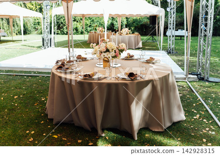 Elegant wedding table setting with floral centerpiece and candles under a marquee tent. Elegant wedding table setting with floral centerpiece and candles under a marquee tent. 142928315