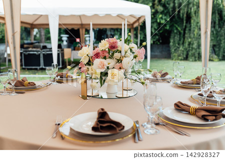 Elegant wedding table setting with floral centerpiece and candles under a marquee tent. Elegant wedding table setting with floral centerpiece and candles under a marquee tent. 142928327