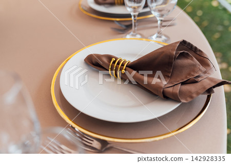 Elegant wedding table setting detail with plates, napkins and golden rings. Elegant wedding table setting detail with plates, napkins and golden rings. 142928335