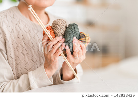 A senior woman holding a ball of yarn and knitting needles. An image of knitting and handicrafts. A senior woman holding a ball of yarn and knitting needles. An image of knitting and handicrafts. 142928429