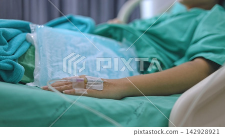 Patient hand with IV saline solution infusion on hospital bed concept. Patient hand with IV saline solution infusion on hospital bed concept. 142928921