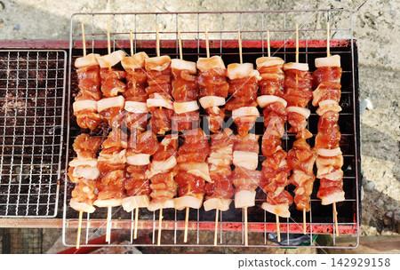 Raw Thai grilled pork skewers (Moo Ping) ready to cook on a barbecue grill. Raw Thai grilled pork skewers (Moo Ping) ready to cook on a barbecue grill. 142929158