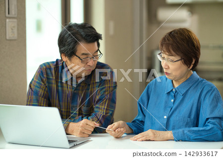 一對老年夫婦一邊看著電腦一邊輸入信用卡資訊。 一對老年夫婦一邊看著電腦一邊輸入信用卡資訊。 142933617