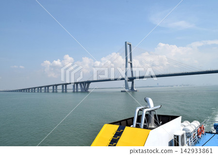 View of a bridge stretching across the sea, connecting two islands against a backdrop of beautiful blue sky and water View of a bridge stretching across the sea, connecting two islands against a backdrop of beautiful blue sky and water 142933861