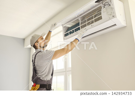 HVAC Technician Servicing Wall Mounted Air Conditioner in Bright Home Interior 142934733
