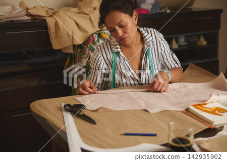 Woman measuring fabric and working on a sewing pattern in a home studio 142935902