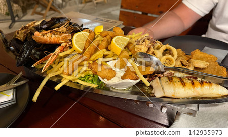 Seafood platter with shrimp, calamari, and fries served on a metal tray at restaurant table Seafood platter with shrimp, calamari, and fries served on a metal tray at restaurant table 142935973