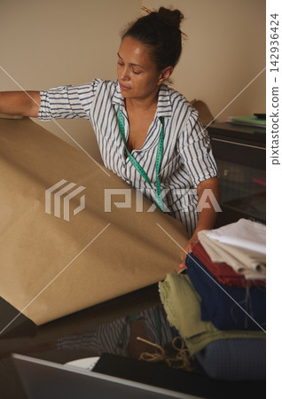 Seamstress at work measuring brown pattern paper with measuring tape in a small sewing workshop Seamstress at work measuring brown pattern paper with measuring tape in a small sewing workshop 142936424