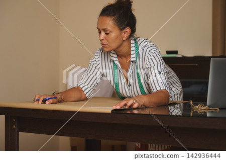 Woman measuring and marking a paper pattern on a table in a home sewing workshop Woman measuring and marking a paper pattern on a table in a home sewing workshop 142936444
