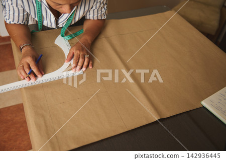 Woman drafting sewing pattern on kraft paper with measuring tape and ruler in a home studio Woman drafting sewing pattern on kraft paper with measuring tape and ruler in a home studio 142936445