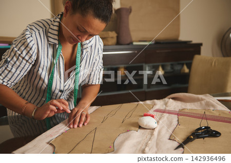 Woman seamstress sewing garment pattern at home workspace with measuring tape and scissors Woman seamstress sewing garment pattern at home workspace with measuring tape and scissors 142936496