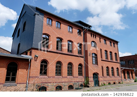 Historic red brick factory building with slate facade under blue sky 142936622