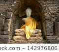 A stone Buddha statue wearing a yellow robe, located in Sukhothai Historical Park in Thailand. 142936806
