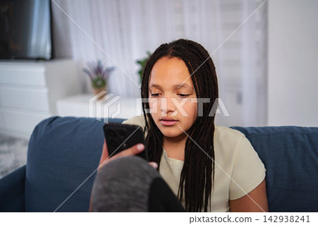 Young girl relaxing on couch browsing smartphone Young girl relaxing on couch browsing smartphone 142938241