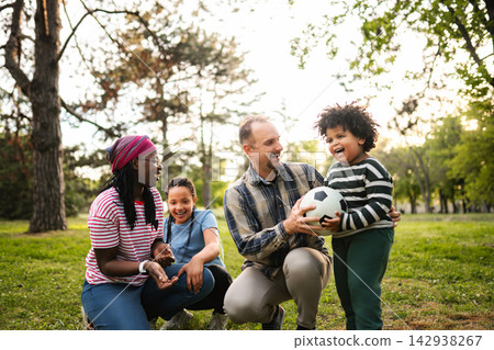 Multiethnic family enjoying afternoon playing soccer ball in park Multiethnic family enjoying afternoon playing soccer ball in park 142938267