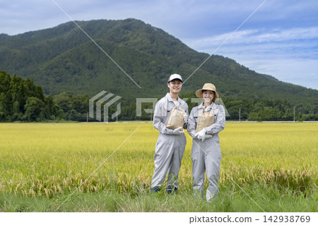 一對面帶微笑的種稻夫婦站在稻田裡,此時正值稻田收割季節。 一對面帶微笑的種稻夫婦站在稻田裡,此時正值稻田收割季節。 142938769