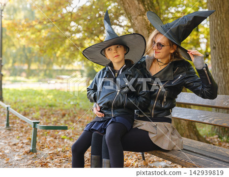 Mother and daughter sitting together on bench during Halloween Mother and daughter sitting together on bench during Halloween 142939819