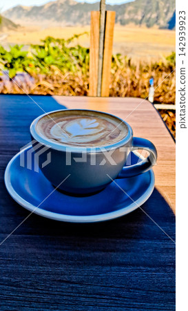A close-up photo of a cup of coffee with Mount Bromo in the background. 142939923