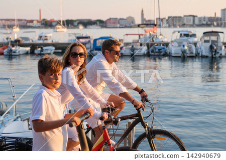 Family Cycling Along Marina Waterfront At Sunset Parents And Son Riding Bicycles By Harbor Family Cycling Along Marina Waterfront At Sunset Parents And Son Riding Bicycles By Harbor 142940679