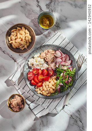 Healthy tuna salad bowl with white beans, feta cheese, tomatoes, radish, and greens on marble table Healthy tuna salad bowl with white beans, feta cheese, tomatoes, radish, and greens on marble table 142940932