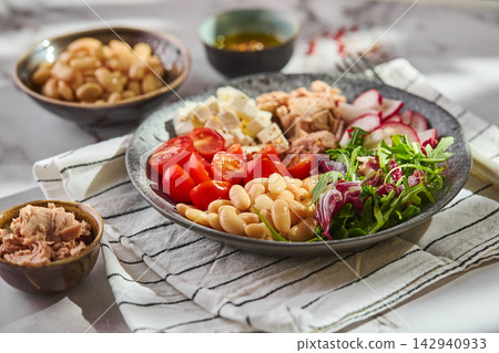 Healthy tuna salad bowl with white beans, feta cheese, tomatoes, radish, and greens on marble table Healthy tuna salad bowl with white beans, feta cheese, tomatoes, radish, and greens on marble table 142940933