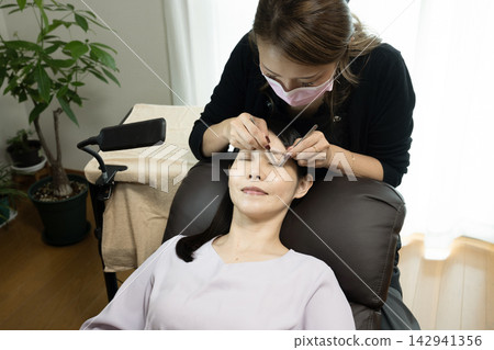 Woman receiving eyelash extension treatment 142941356