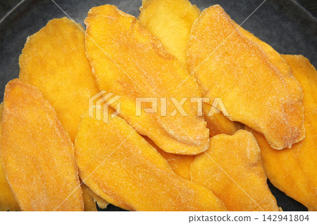 Slices of dried mango on black background. Macro photo 142941804