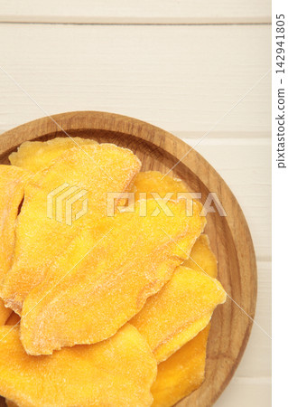 Slices of dried mango on wooden plate on light wooden background. Vertical photo Slices of dried mango on wooden plate on light wooden background. Vertical photo 142941805