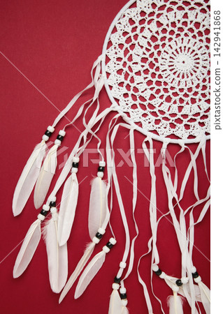Handmade dream catcher hanging on a rope with feathers, threads, and beads on red background. Handmade dream catcher hanging on a rope with feathers, threads, and beads on red background. 142941868