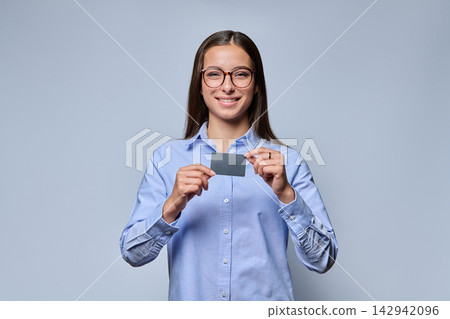 Smiling young woman in blue shirt holding black plastic card studio shot Smiling young woman in blue shirt holding black plastic card studio shot 142942096