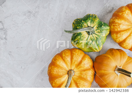 Green and orange pumpkins arranged in corner position on smooth marble background representing autumn harvest variety for seasonal grocery or culinary design Green and orange pumpkins arranged in corner position on smooth marble background representing autumn harvest variety for seasonal grocery or culinary design 142942386