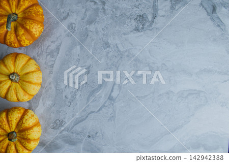 Miniature orange pumpkins line up along edge of natural gray marble table background with wide copy space reserved for autumn marketing text or holiday menu Miniature orange pumpkins line up along edge of natural gray marble table background with wide copy space reserved for autumn marketing text or holiday menu 142942388