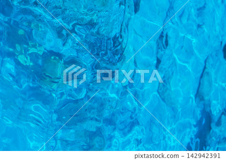 Clear blue water surface ripple background showing bright sunlight reflections inside swimming pool or tropical ocean for summer vacation or spa wellness relaxation 142942391