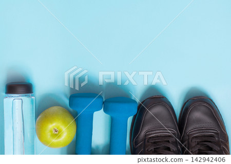 Sport and fitness equipment with sneakers, dumbbells on blue. Top view, space for your text. Sport and fitness equipment with sneakers, dumbbells on blue. Top view, space for your text. 142942406