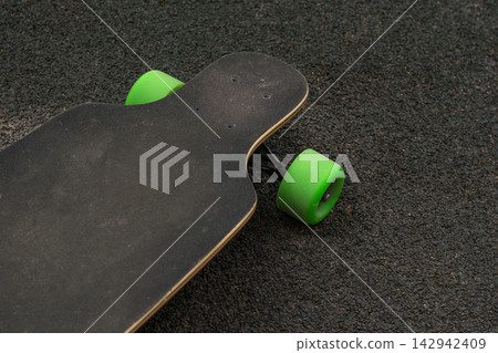 Old used skateboard isolated on the ground. Old style longboard. Black skateboard on an empty asphalt road. Old used skateboard isolated on the ground. Old style longboard. Black skateboard on an empty asphalt road. 142942409