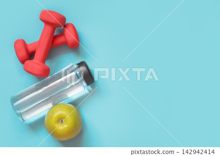 Sport and fitness equipment, dumbbells, water and apple. Creative flat lay on punchy blue. Space for your text. 142942414