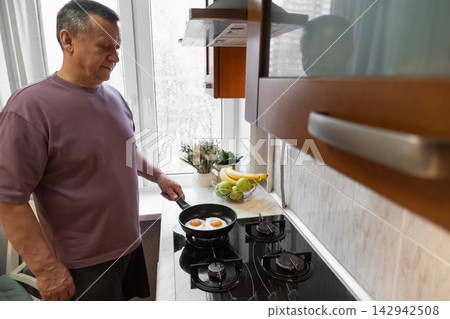 Senior man cooking fried eggs for breakfast at home Senior man cooking fried eggs for breakfast at home 142942508