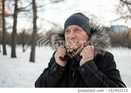 Mature man adjusting warm coat in snowy winter park Mature man adjusting warm coat in snowy winter park 142942513