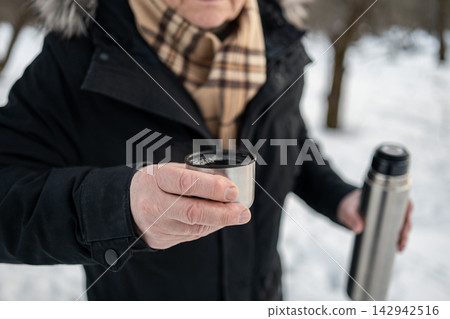 Mature man offering cup of hot drink outdoors in winter Mature man offering cup of hot drink outdoors in winter 142942516