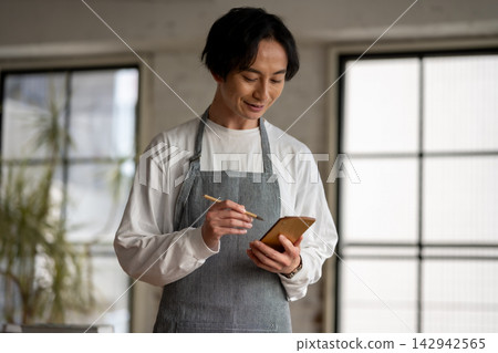 A man in an apron is working with a smile on his face, writing in a notepad. A man in an apron is working with a smile on his face, writing in a notepad. 142942565