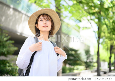 一位戴著草帽、背著背包的女子抬頭望著綠樹成蔭的街道。 一位戴著草帽、背著背包的女子抬頭望著綠樹成蔭的街道。 142942652