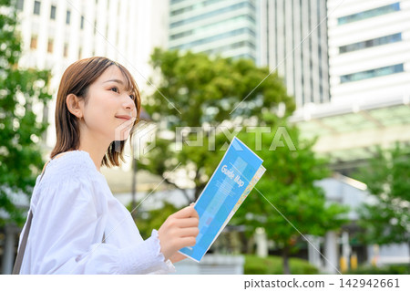 一位年輕女子看著地圖,欣賞著城市景觀。 一位年輕女子看著地圖,欣賞著城市景觀。 142942661
