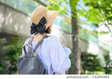 一位頭戴草帽、背著背包的女子漫步在綠樹成蔭的街道上。 一位頭戴草帽、背著背包的女子漫步在綠樹成蔭的街道上。 142942664