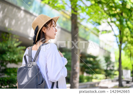 一位背著背包、頭戴草帽的女子漫步在綠樹成蔭的街道上。 一位背著背包、頭戴草帽的女子漫步在綠樹成蔭的街道上。 142942665