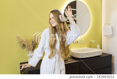 Happy woman in headphones singing and dancing in modern bathroom at home 142943032