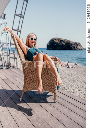 Blonde mature woman enjoying a sunny day sitting in a wicker chair at the seaside resort 142945016