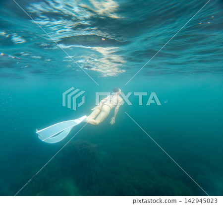 Underwater freediving woman swimming with white monofin in clear turquoise ocean depths Underwater freediving woman swimming with white monofin in clear turquoise ocean depths 142945023