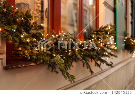 Cozy Christmas window display decorated with glowing lights and garland Cozy Christmas window display decorated with glowing lights and garland 142945133