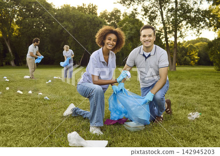 Happy volunteers collecting park litter in gloves, teamwork for clean green spaces Happy volunteers collecting park litter in gloves, teamwork for clean green spaces 142945203
